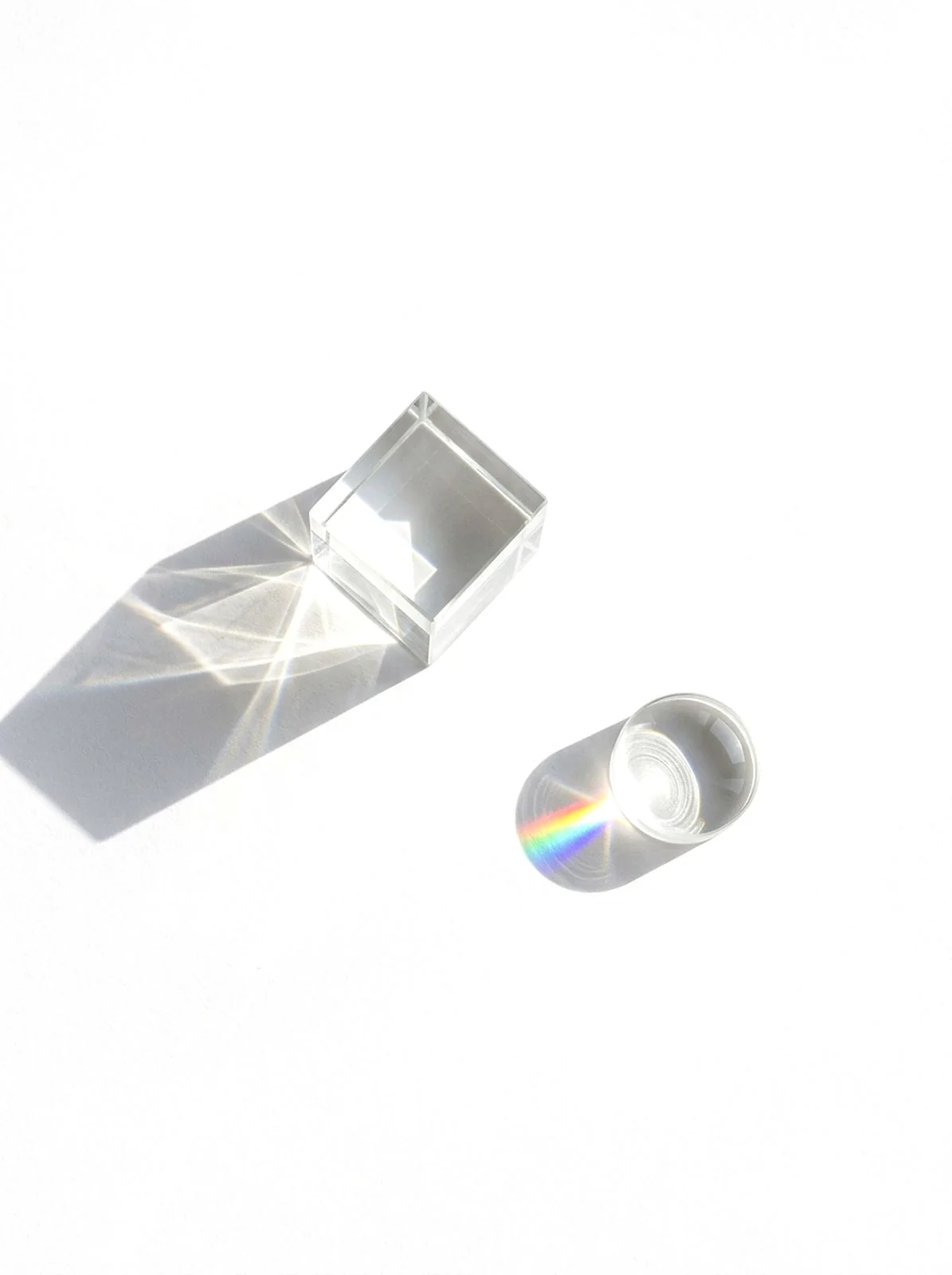 Clear optical objects casting geometric light onto a pale surface.